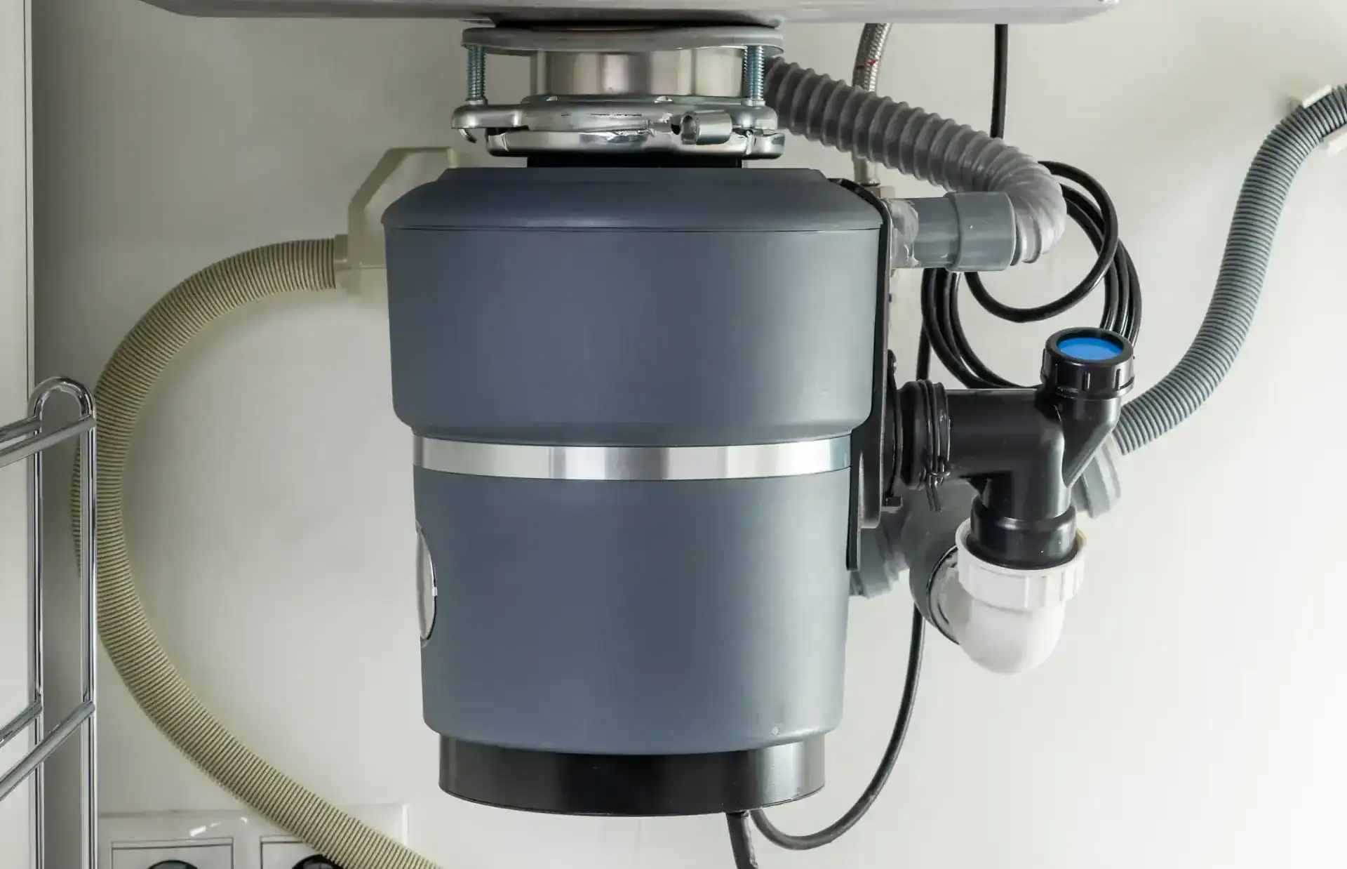 A close-up view of a garbage disposal unit installed under a kitchen sink, showing various connected pipes and hoses—ideal for those seeking a plumber in Pasco County, FL.