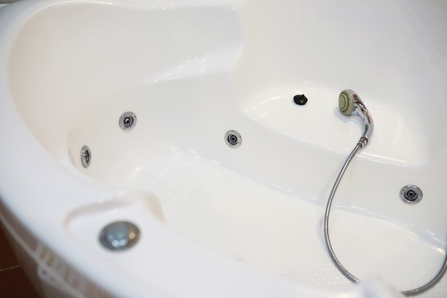 White bathtub with built-in jets and a handheld showerhead is shown resting on the tub floor.